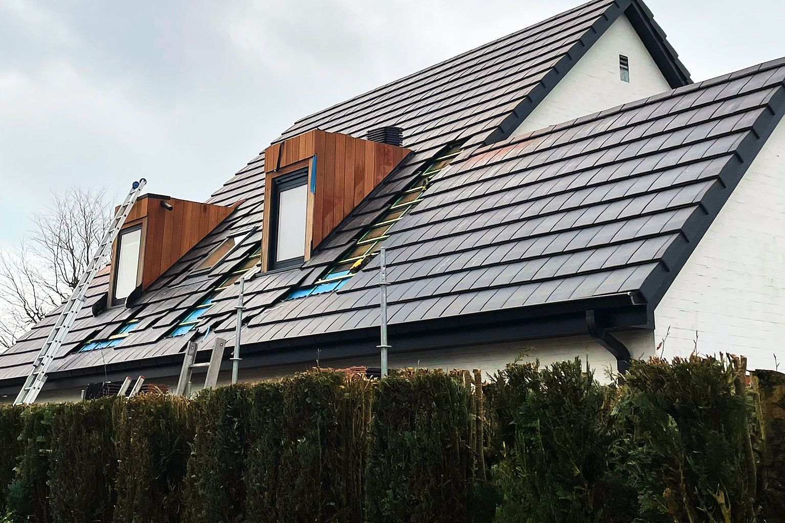 Een nieuw dak in vlakke, donkere dakpannen met twee dakkapellen in hout.