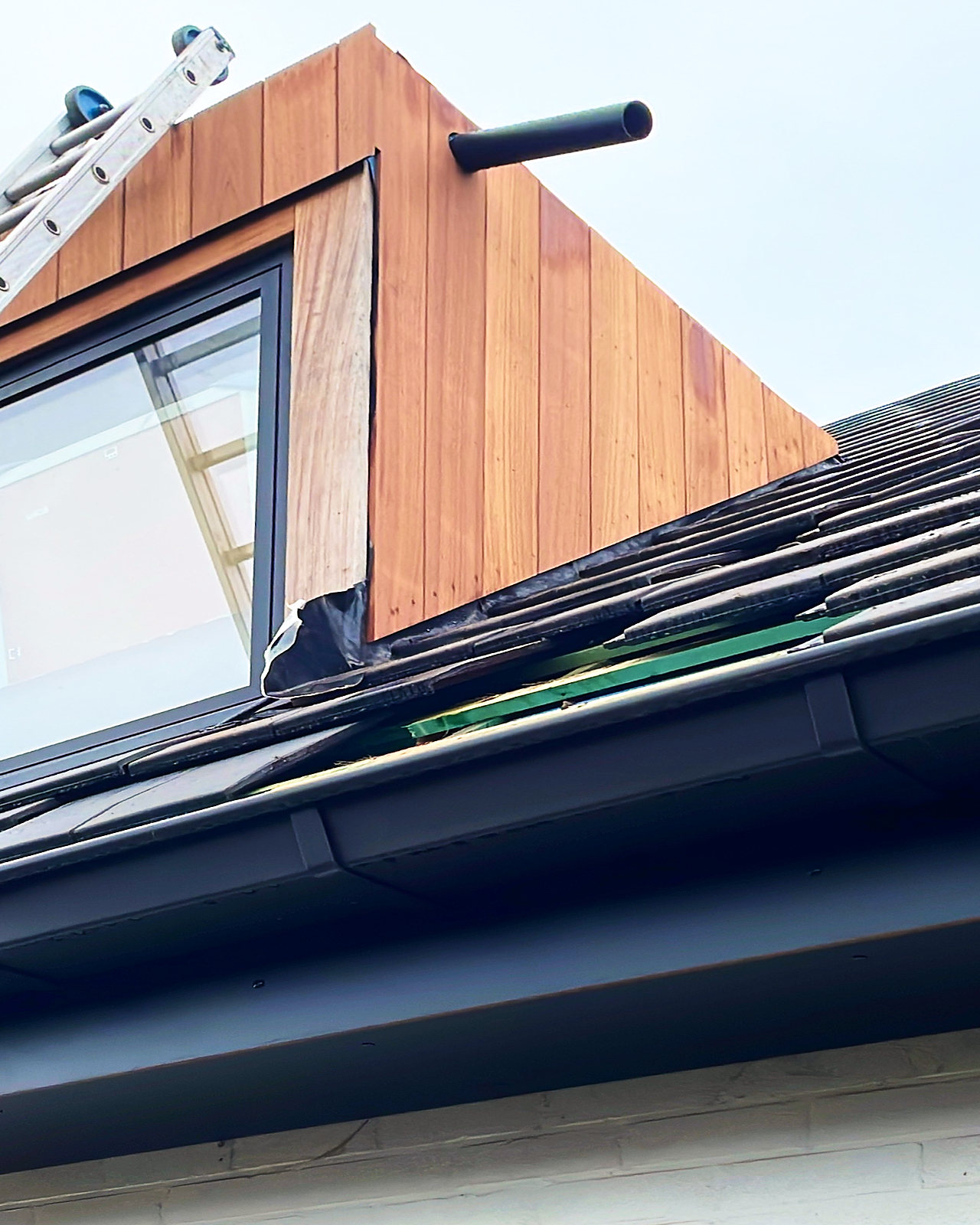 Detail van een dakkapel met houten bekleding, boven een nieuwe zwarte dakgoot.