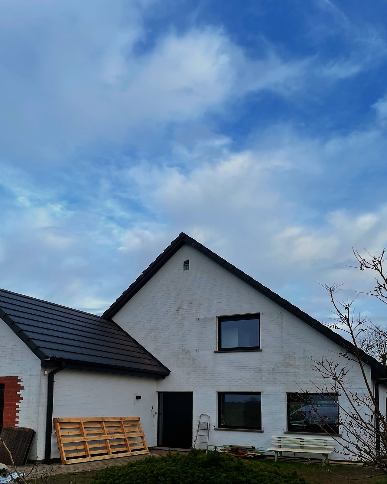 De witte woning met het nieuwe donkere dak, twee dakkapellen in hout en zwarte goten en afvoerbuizen.