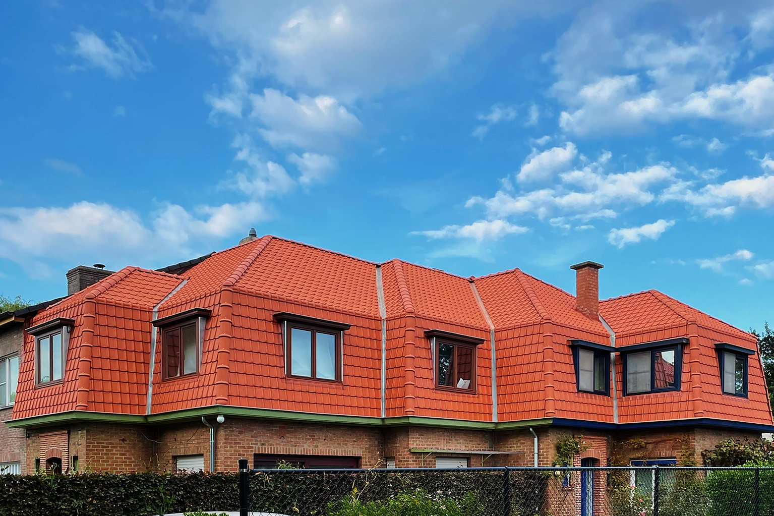 Een woning met een volledig vernieuwd mansardedak in natuurrode stormpannen en dakkapellen in zink, na de renovatie door Vlerick Dakwerken.