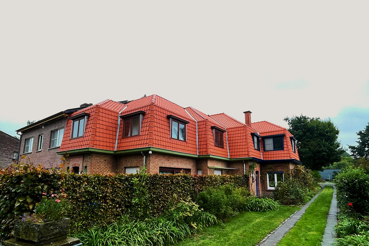 Zijaanzicht van de gerenoveerde woning: rode stormpannen, vijf dakkapellen en een bakstenen schoorsteen.