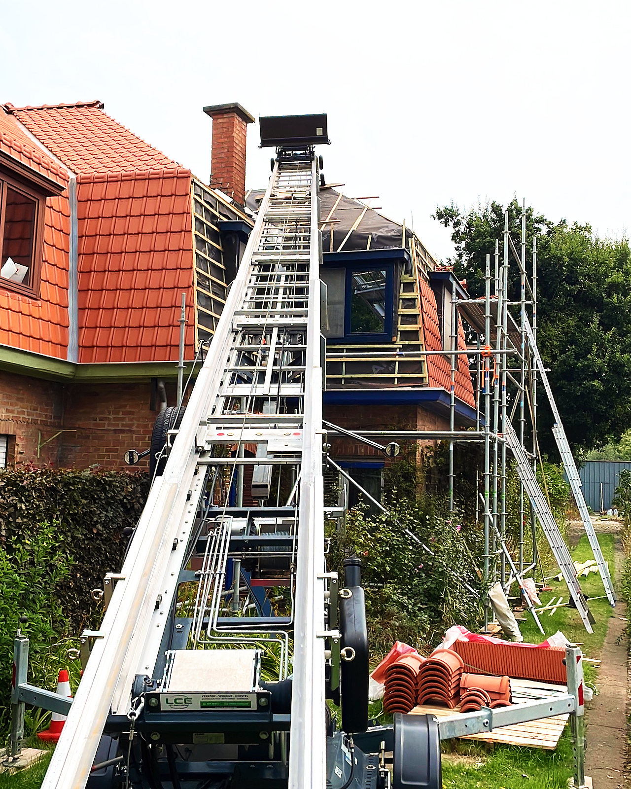 Werf tijdens de renovatie: een ladderlift en een stelling tegen de woning, met het pannendak deels gelegd.