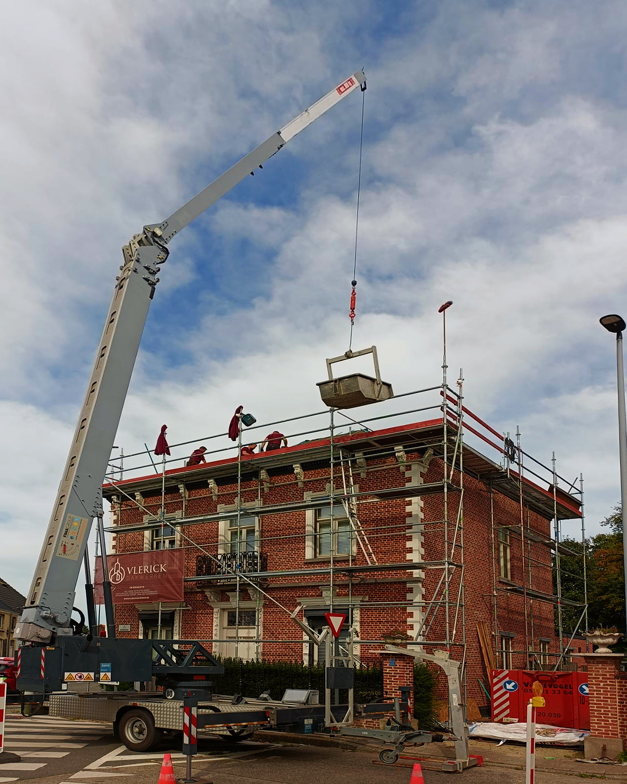 De kraan brengt materiaal naar het dak van het herenhuis.
