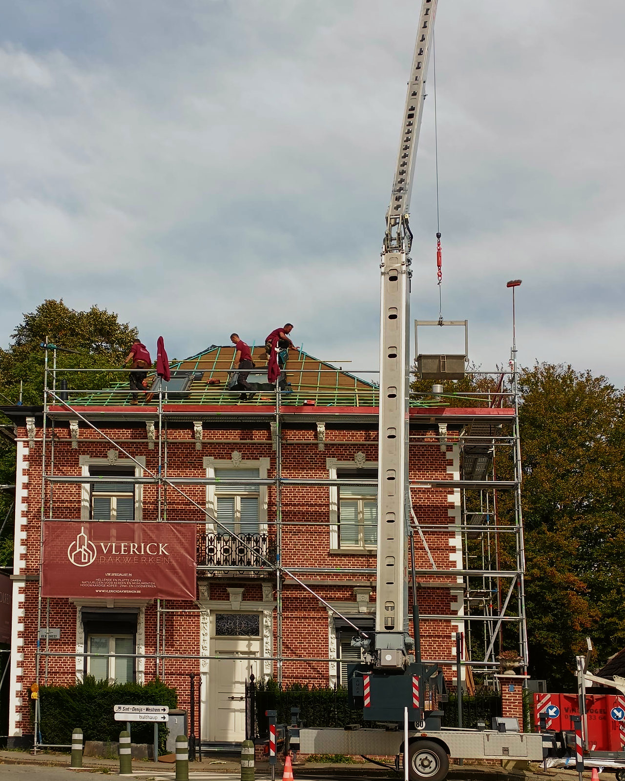 Vakmannen aan het werk op het dak, met de kraan naast de woning.