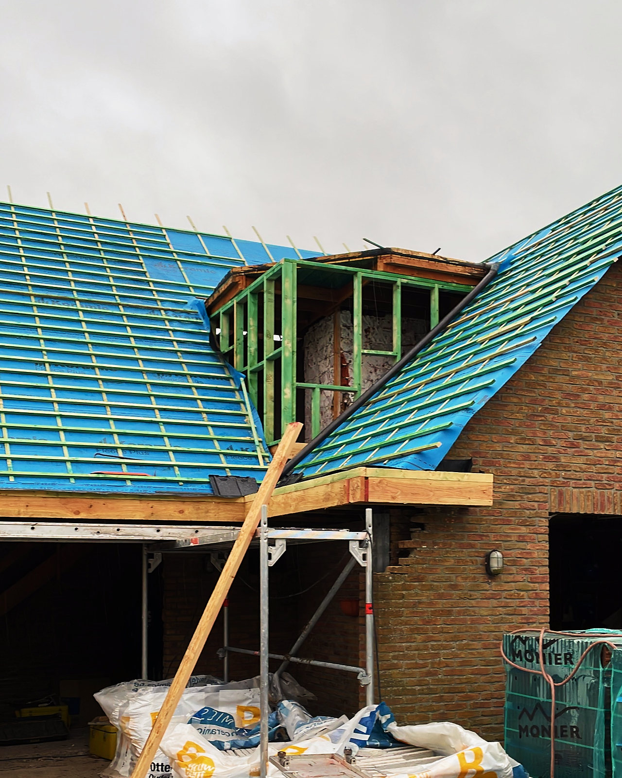 Dakvlakken met nieuw blauw onderdak en panlatten, met in het midden het houten skelet van een dakkapel.