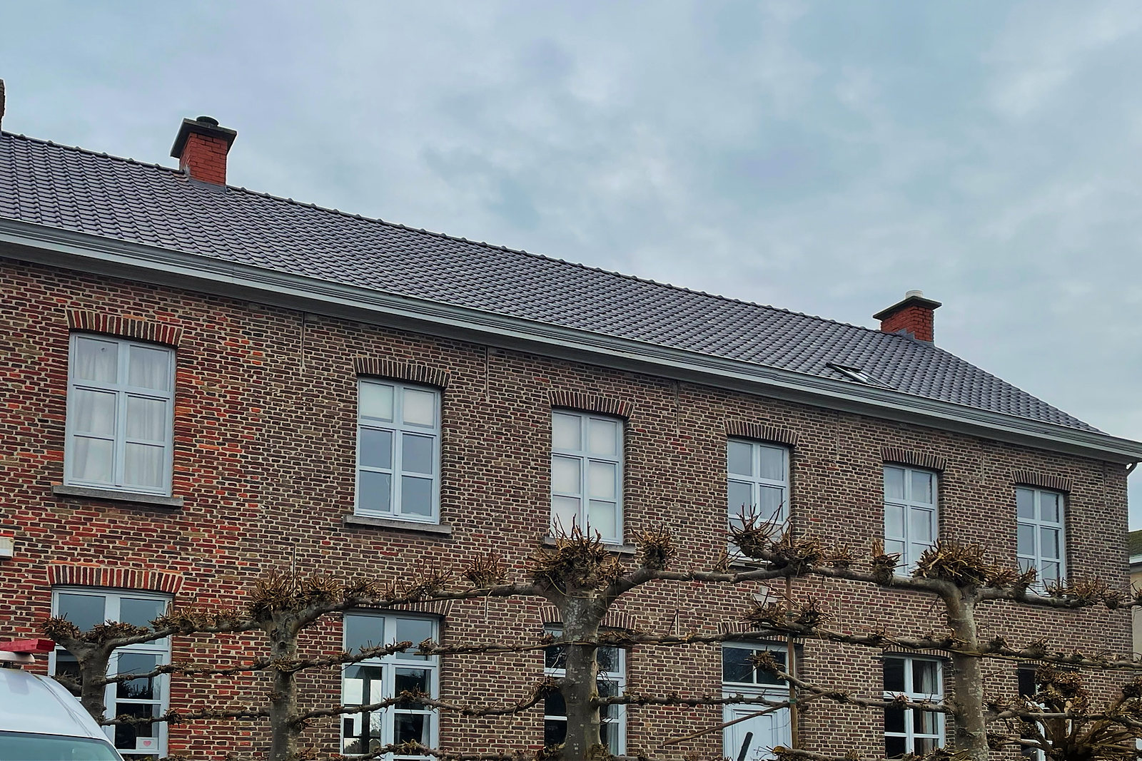Een groot bakstenen herenhuis met leilindes voor de gevel en een volledig nieuw dak in grijze pannen.