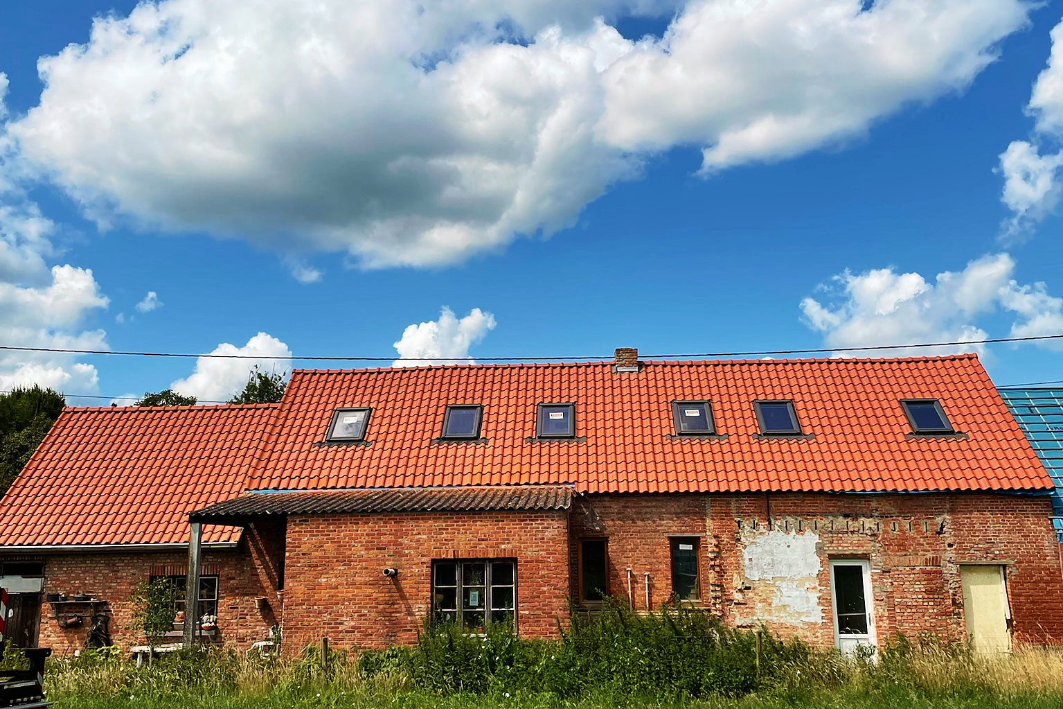 De langgevelboerderij met een volledig nieuw dak in rode pannen en een rij dakramen.