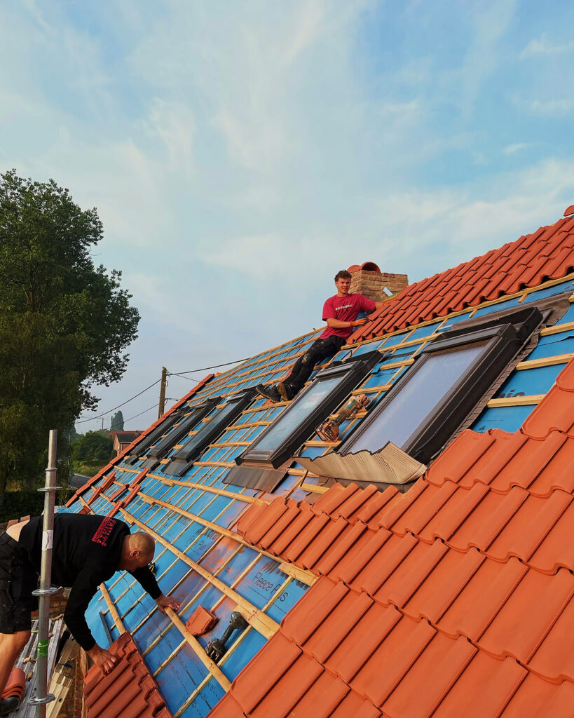 Vakmannen leggen de rode pannen rond de nieuwe dakramen.