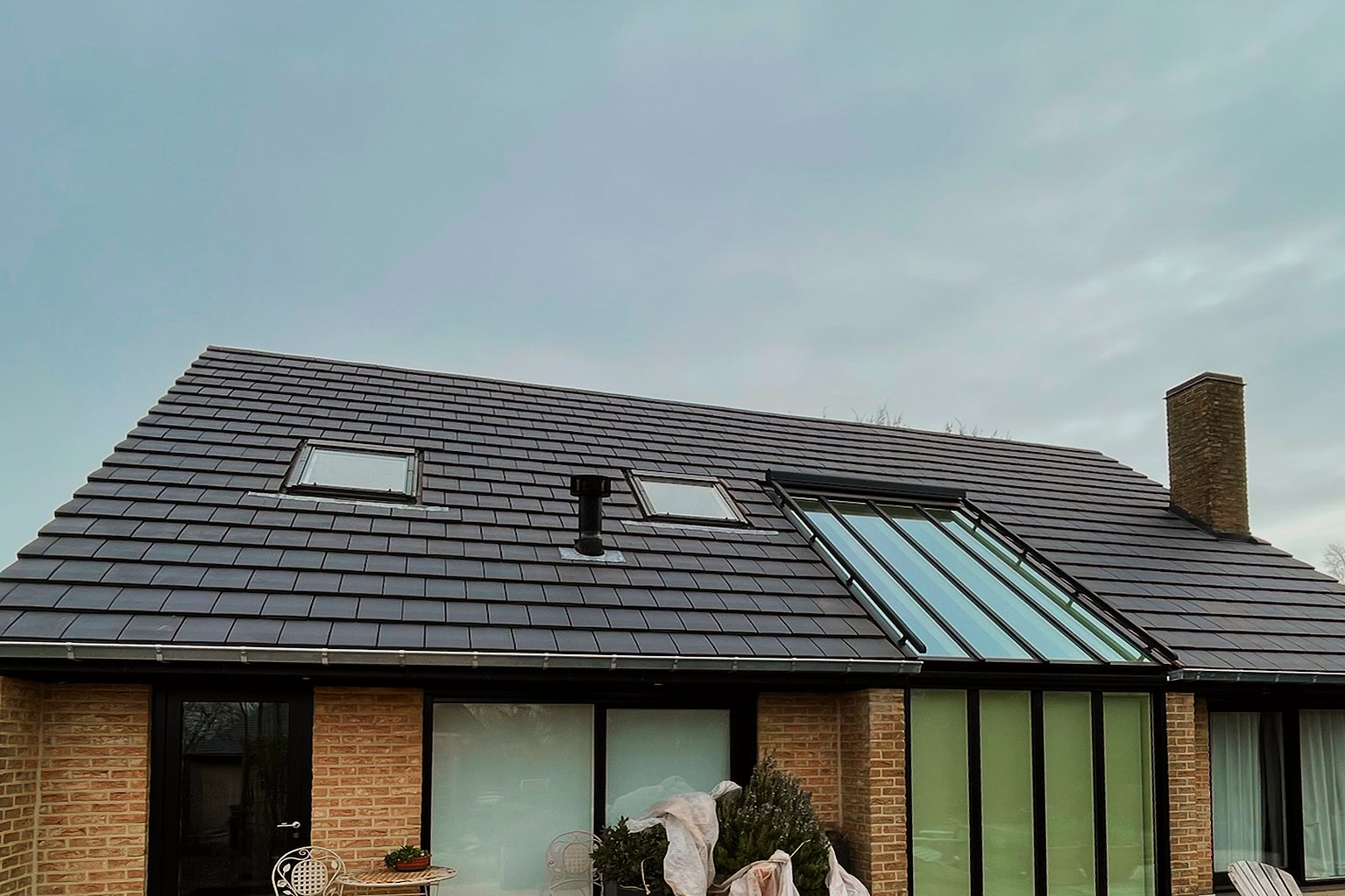 De achtergevel van de woning met het nieuwe dak in vlakke, donkere pannen, dakramen en het glazen dakdeel.