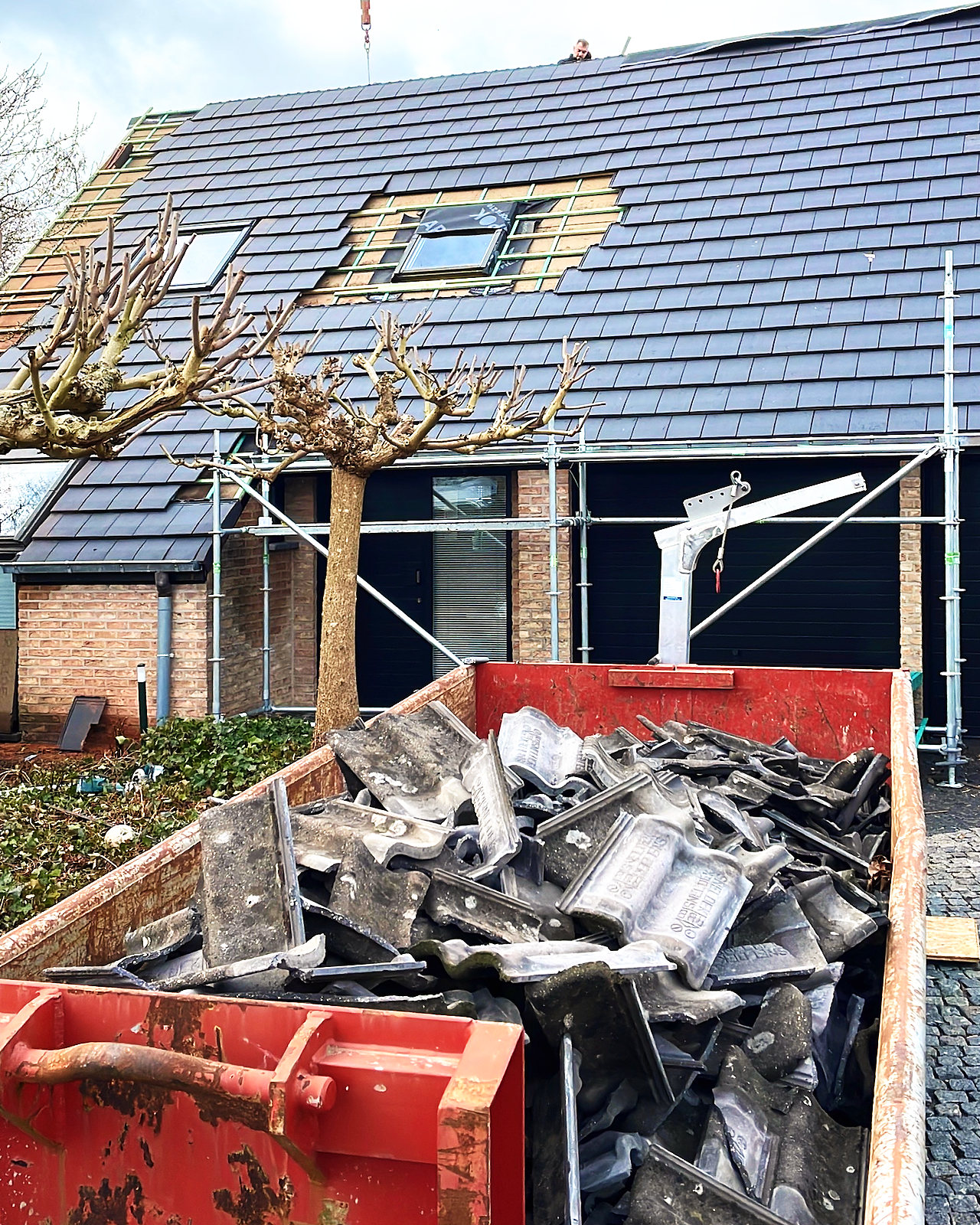 De oude dakpannen liggen in een container naast de woning in de stelling.