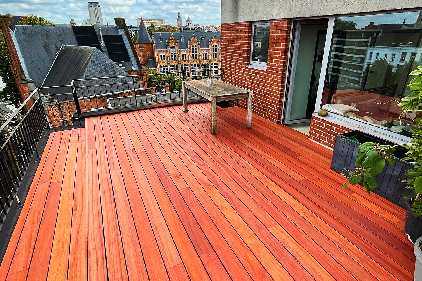 Afgewerkt dakterras in padoekhout op een vernieuwd plat dak, met een balustrade en zicht over de stad.